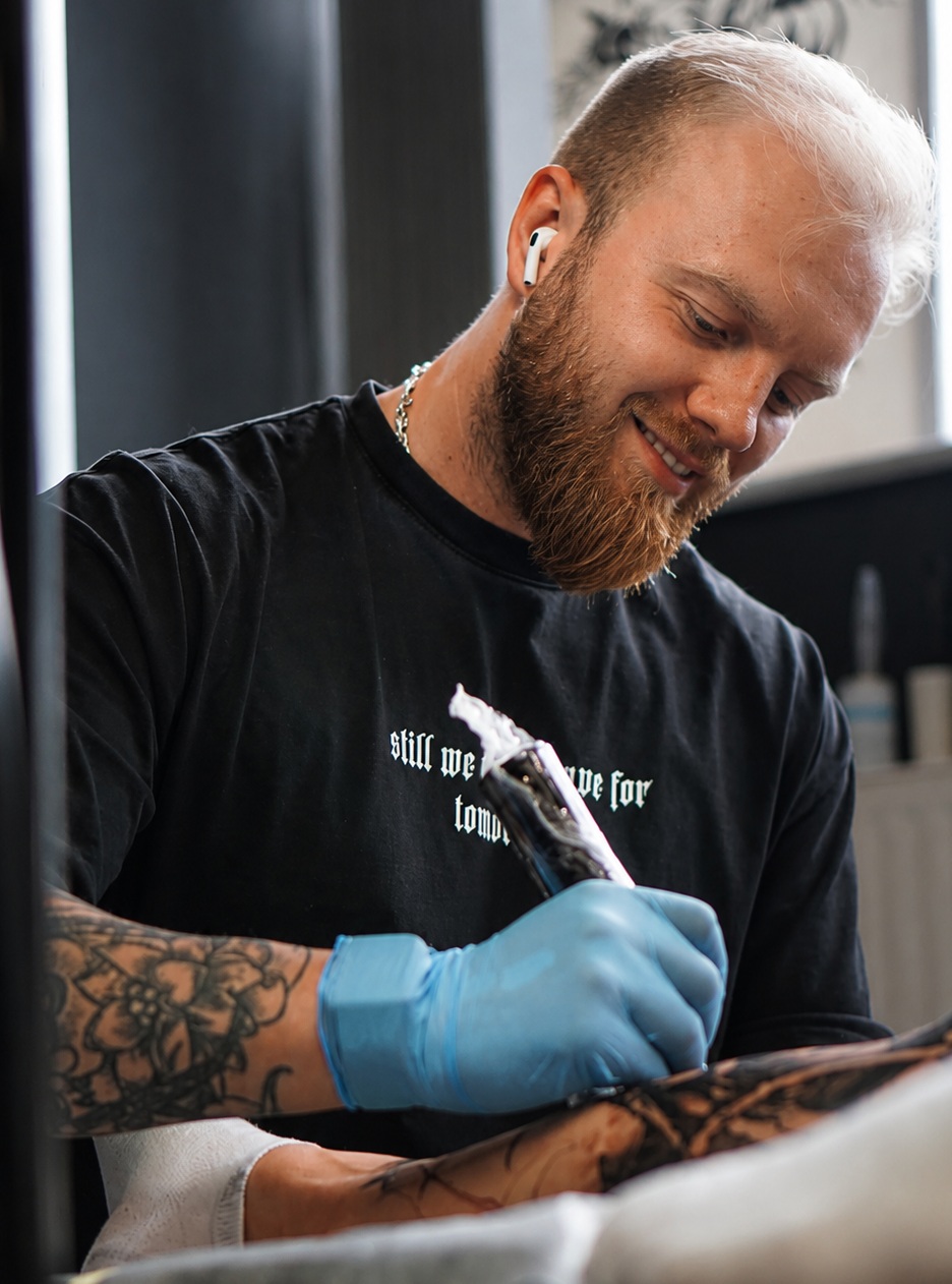 Tatuator w rękawiczkach wykonujący tatuaż klientowi
